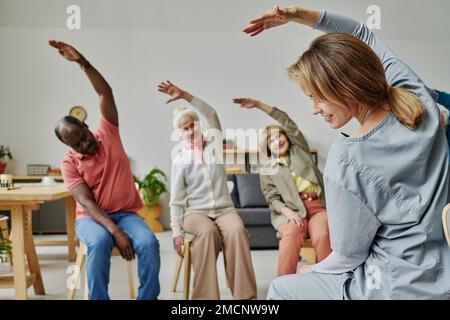 Vista posteriore di giovani istruttori che fanno esercizi insieme a persone anziane durante la formazione mattutina Foto Stock