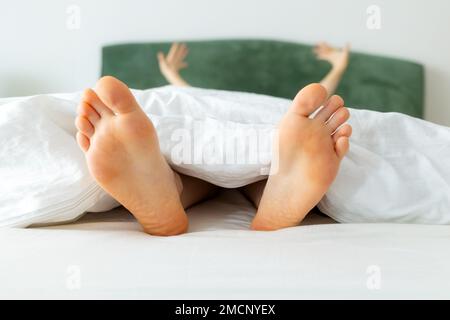 Femmina a piedi nudi in primo piano. Donna divertente stretching sdraiato sul letto. Biancheria da letto bianca. Suole asciutte. Concetto di vacanza e riposo. Foto Stock