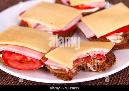 Su un piatto bianco, ammollate il panino con pane di segale, pomodori, prosciutto e formaggio Foto Stock