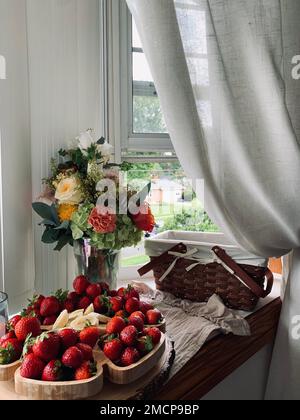 Un colpo verticale di un mazzo di banane e fragole affettate sulla sporgenza della finestra con un bouquet Foto Stock