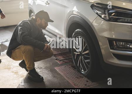 Controllo meccanico della geometria e della sospensione di una ruota di un'auto con attrezzi di precisione. Foto di alta qualità Foto Stock