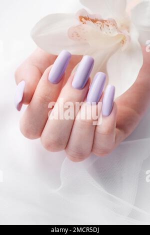 Mani di ragazza con delicata manicure viola e fiori di orchidea. Il concetto di bellezza e cura del corpo. Foto Stock