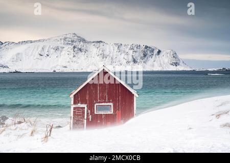 Rorbuer rosso capanna di pesca sulla spiaggia nella neve, Ramberg, Flakstadoya, Lofoten, Norvegia Foto Stock