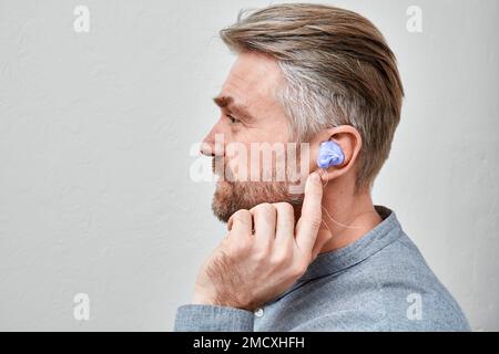 Creazione di stampi auricolari personalizzati. Uomo con materiale siliconico nell'orecchio, mentre processo di realizzazione di auricolari personalizzati per il suo apparecchio acustico in clinica audiologica Foto Stock