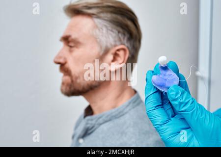 Audiologo che tiene in mano singoli auricolari sagomati per apparecchi acustici del paziente, primo piano. Auricolari personalizzati per apparecchi acustici Foto Stock