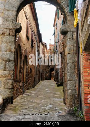 Scena di strada medievale, antico cortile pavimentato in pietra con ingresso ad arco in pietra Roccatederighi, Toscana, Italia, Foto Stock