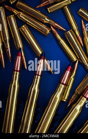 Munizioni per la mitragliatrice e fucile sono sparsi sul tavolo. Ammonuizione su tavolo blu scuro. Munizioni pila, sfondo di munizioni di guerra Foto Stock