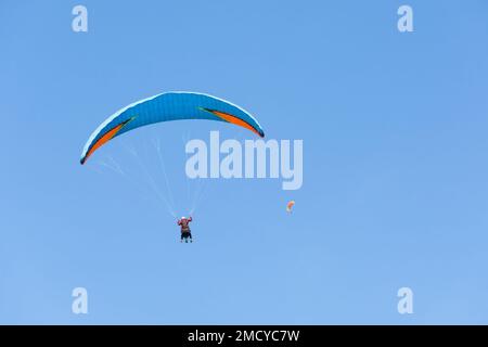 Due parapendio tandem volano contro il cielo blu, parapendio tandem a distanza guidato da un pilota Foto Stock