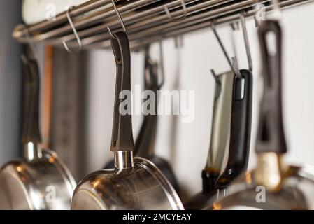 Padelle e utensili da cucina appendono su ganci in cucina. Deposito di utensili da cucina. Foto Stock