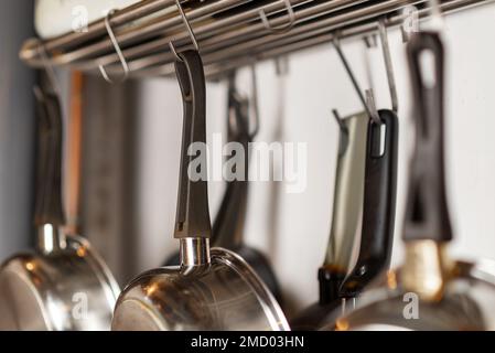 Padelle e utensili da cucina appendono su ganci in cucina. Deposito di utensili da cucina. Foto Stock