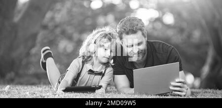 Banner di padre su figlio ragazzo scuola con notebook studio online giacente su erba, formazione online su laptop. padre e figlio usano la comunicazione moderna Foto Stock