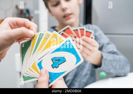 Minsk, Bielorussia 08.01.23 foto ritagliata di due ragazzi amici bambini seduti al tavolo in cucina a casa, tenendo carte di gioco di carte uno, tavolo da gioco Foto Stock