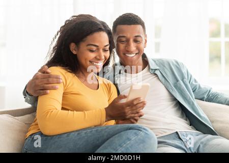 Felice giovane afro americano ragazzo e donna guardare il telefono, avere videochiamata, guardare video Foto Stock