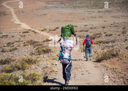 Un portiere che porta un carico pesante sulla schiena cammina lungo la strada. Foto Stock