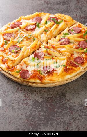 Pizza americana con patatine fritte, salsicce, formaggio, salsa di pomodoro base primo piano su un asse di legno sul tavolo. Verticale Foto Stock