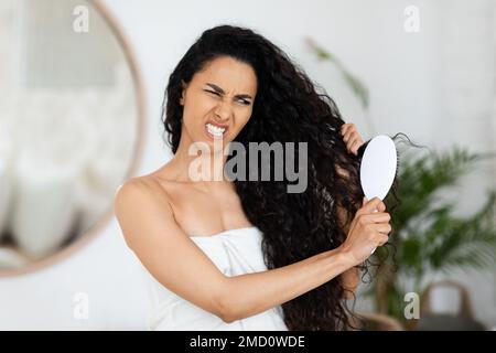 Infelice triste donna araba millenaria ricci in asciugamano pettinandole capelli asciutti, aggrovigliati dopo la doccia Foto Stock