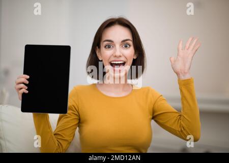Giovane donna entusiasta che mostra un tablet con schermo nero Foto Stock