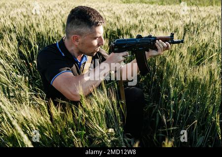 L'uomo sul campo con una mitragliatrice, gli uomini ucraini si stanno preparando alla guerra, il fucile automatico di Kalashnikov. Foto Stock