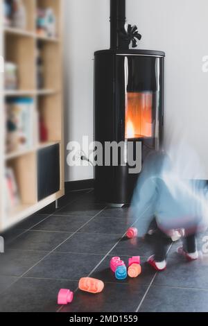 Stufa a pellet con un bambino che gioca in sicurezza davanti, con fiamme e biblioteca Foto Stock