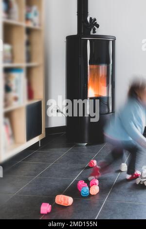 Stufa a pellet con un bambino che gioca in sicurezza davanti, con fiamme e biblioteca Foto Stock