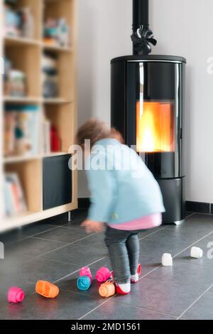 Stufa a pellet con un bambino che gioca in sicurezza davanti, con fiamme e biblioteca Foto Stock