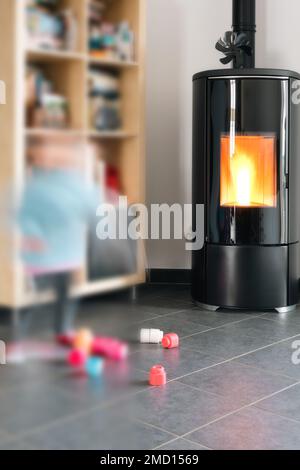 Stufa a pellet con un bambino che gioca in sicurezza davanti, con fiamme e biblioteca Foto Stock