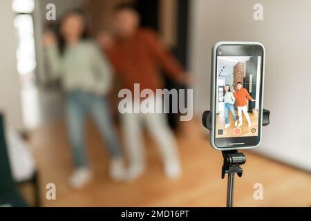 Marito e moglie asiatici che registrano contenuti video per i social media, ballano di fronte alla fotocamera del cellulare, messa a fuoco selettiva Foto Stock
