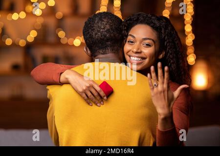 Allegra donna nera che mostra l'anello di fidanzamento, abbracciando la sua fidanzata Foto Stock