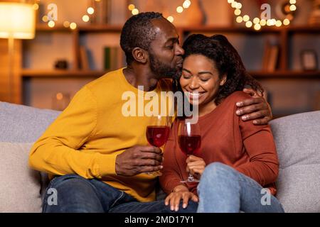 Grazie. Primo piano di una bella giovane coppia americana sorridente che beve vino rosso, che tiene bicchieri e brinda, che cena romantica, che trascorre del tempo Foto Stock