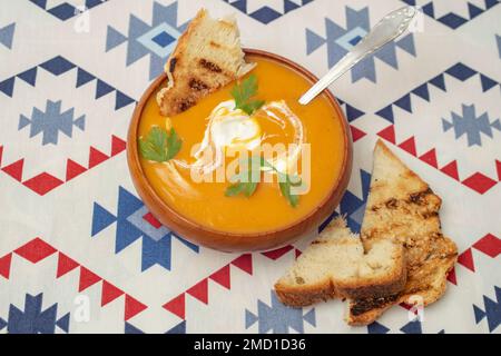 Zuppa di zucca con foglie di prezzemolo, panna acida e pane tostato in un recipiente di legno, fuoco morbido Foto Stock