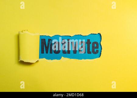 Motivare scritto con lettere di timbro su carta blu con sfondo giallo strappato. Primo piano con messa a fuoco morbida Foto Stock