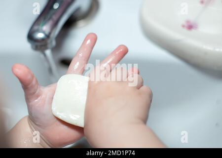 pezzo di sapone bianco nelle mani del bambino piccolo. il bambino lava le mani e si lava Foto Stock