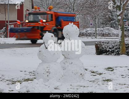 22 gennaio 2023, Sassonia-Anhalt, Wernigerode: Un veicolo del servizio invernale passa dietro due snowmen in piedi in una zona residenziale. In gran parte dei monti Harz ci sono state forti nevicate nella notte alla domenica. Foto: Matthias Bein/dpa Foto Stock