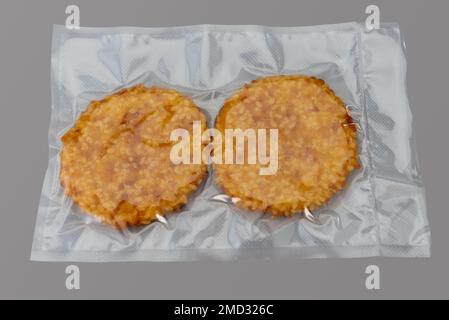 Hamburger impanato con filetto di pollo confezionato sottovuoto sigillato per una cucina sous vide isolata su sfondo grigio in vista dall'alto Foto Stock