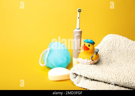 Articoli da bagno. Spazzolino elettrico, asciugamano bianco, panno blu, sapone bianco, anatra di gomma per fare il bagno su sfondo giallo Foto Stock