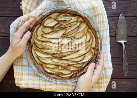 Le mani femminili tengono cotta torta di pere su un tavolo rustico in legno, stile vintage, vista dall'alto. Foto Stock