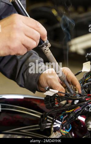 Un elettricista sta saldando i fili elettrici alle apparecchiature elettriche di una motocicletta. Primo piano. Concetto di trasporto Foto Stock