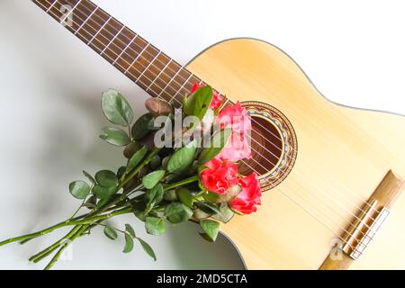 Chitarra classica e rose rosse su sfondo bianco. Foto Stock