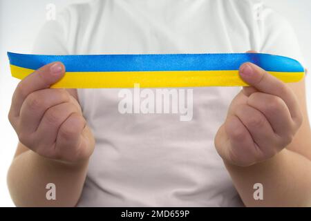 Una ragazza in una T-shirt bianca tiene un nastro giallo-blu nelle sue mani (primo piano). Bandiera dello Stato dell'Ucraina. Simbolo nazionale dell'Ucraina. Patriot Foto Stock