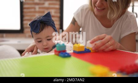 Donna e bambino che giocano con blocchi di costruzione seduti sul tavolo all'asilo Foto Stock