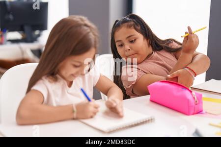 Due studenti bambini seduti sul tavolo disegnando su un foglio di carta in classe Foto Stock