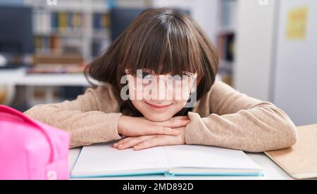 Adorabile ragazza ispanica studente seduto sul tavolo appoggiato al libro in classe Foto Stock
