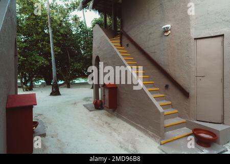 Villa in terracotta tropicale con ingresso con pavimento in sabbia, un utensile antincendio rosso e ciotola per il lavaggio dei piedi, highl a strisce gialle Foto Stock
