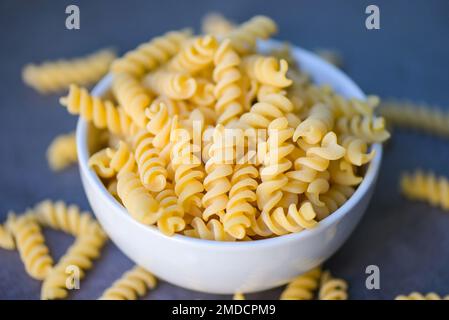 Pasta cruda maccheroni su ciotola bianca, primo piano macaroni crudo pasta a spirale cruda cruda deliziosa pasta fusilli per cucinare i cibi Foto Stock