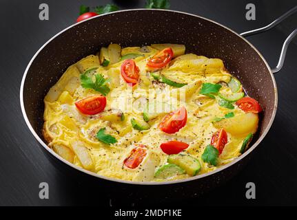 Omelette con pomodori, zucchine e patate su fondo scuro. Dieta sana per la colazione. Gustoso cibo del mattino. Foto Stock