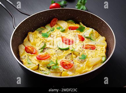 Omelette con pomodori, zucchine e patate su fondo scuro. Dieta sana per la colazione. Gustoso cibo del mattino. Foto Stock