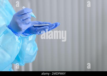 Mani del medico che eseguono analisi antigeniche del campione di liquido indossando dispositivi di protezione individuale completi Foto Stock