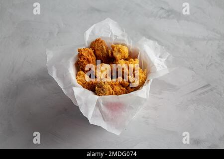Popcorn di pollo, ali, aste in scatola di carta su sfondo grigio, vista laterale. Foto Stock