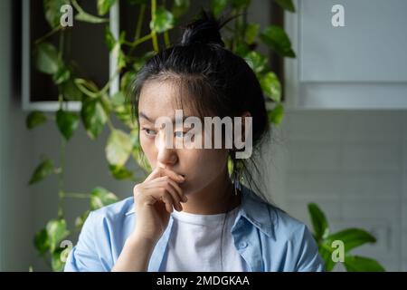 Donna asiatica malinconica premurosa tocca le labbra con la mano sperimentando disturbo psicologico Foto Stock