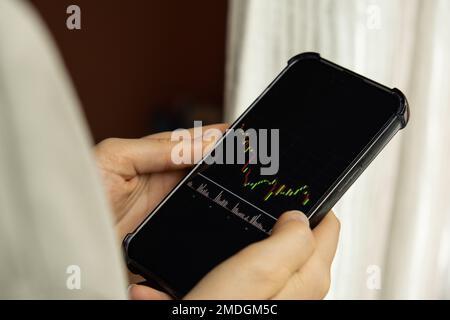 Mani femminili che tengono il telefono, controllando il grafico del mercato azionario per il tranding e l'investimento nel cambio di sicurezza. Donna in attesa di telefono Visualizza la schermata dell'indice delle azioni. Concetto di investimento di mercato azionario contabilità Finanza Foto Stock